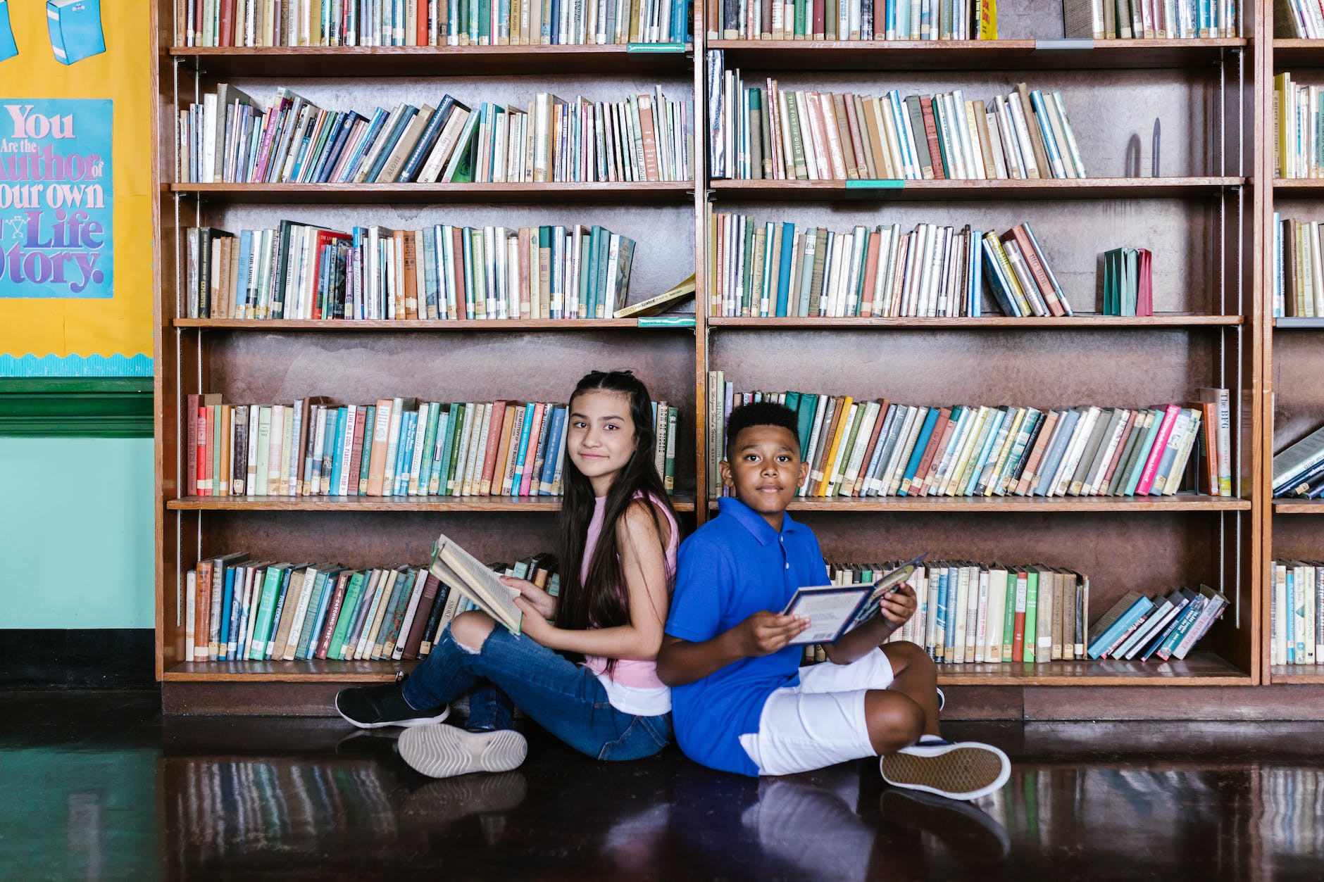 a boy and girl sitting on the floor while holding books