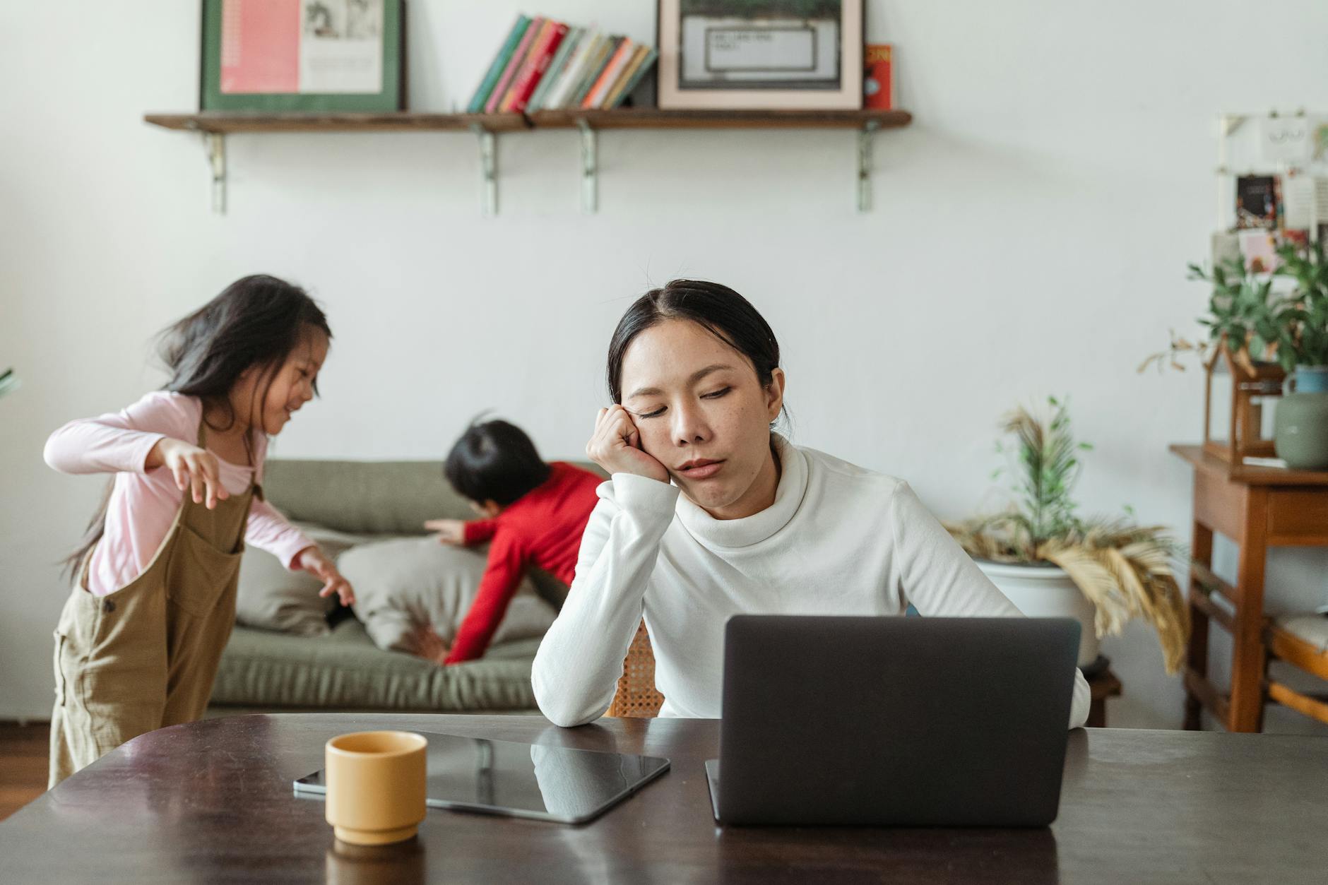 tired ethnic working mother at home with playing kids